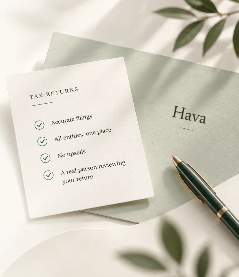 A sage envelope marked Hava on a cream desk, with a forest-green fountain pen beside it and olive leaves across the light.